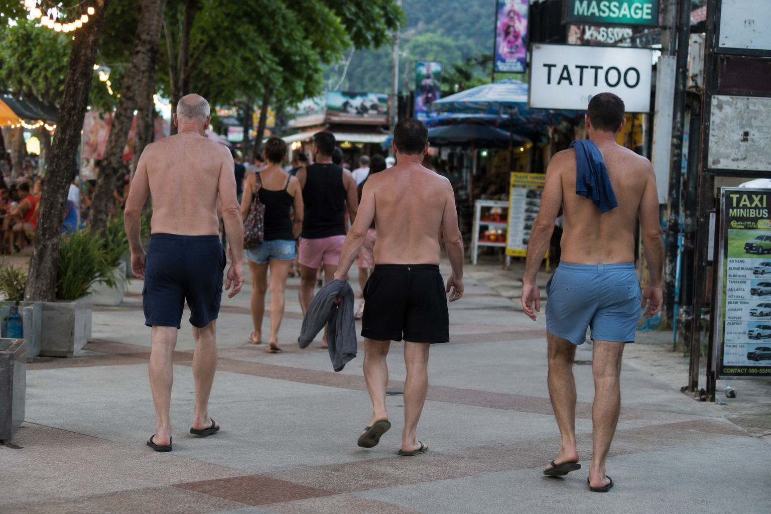 Tourists walking shirtless through a busy street in Thailand away from the beach area