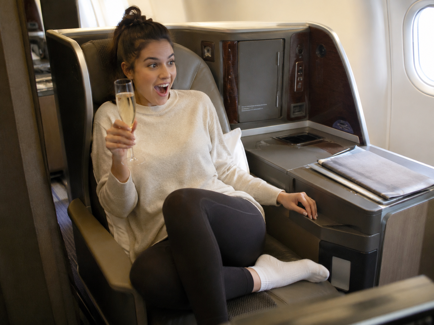 Happy woman surprised after receiving a free business class upgrade while drinking prosecco on a flight
