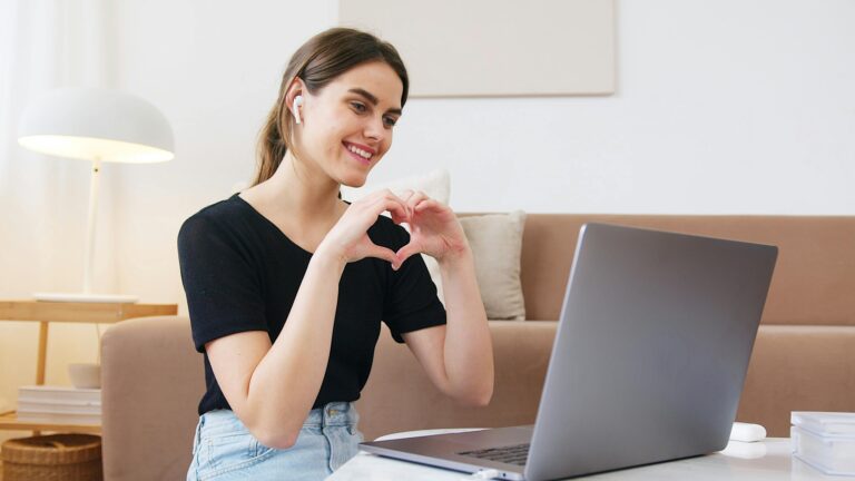 Woman making a heart sign during an online video relationship call on a laptop at home