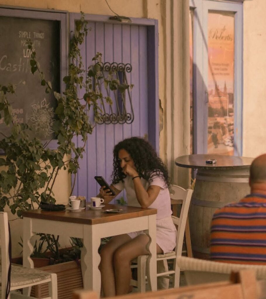 Young woman sitting alone in a cafe looking at her phone, representing modern digital communication and phone anxiety