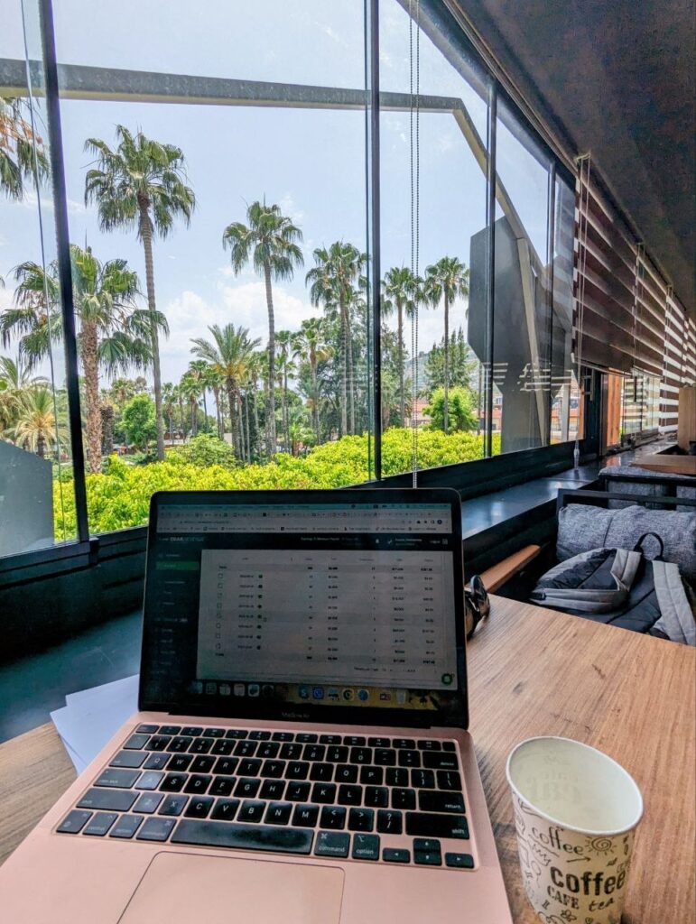 Laptop and coffee at a café workspace with palm tree view