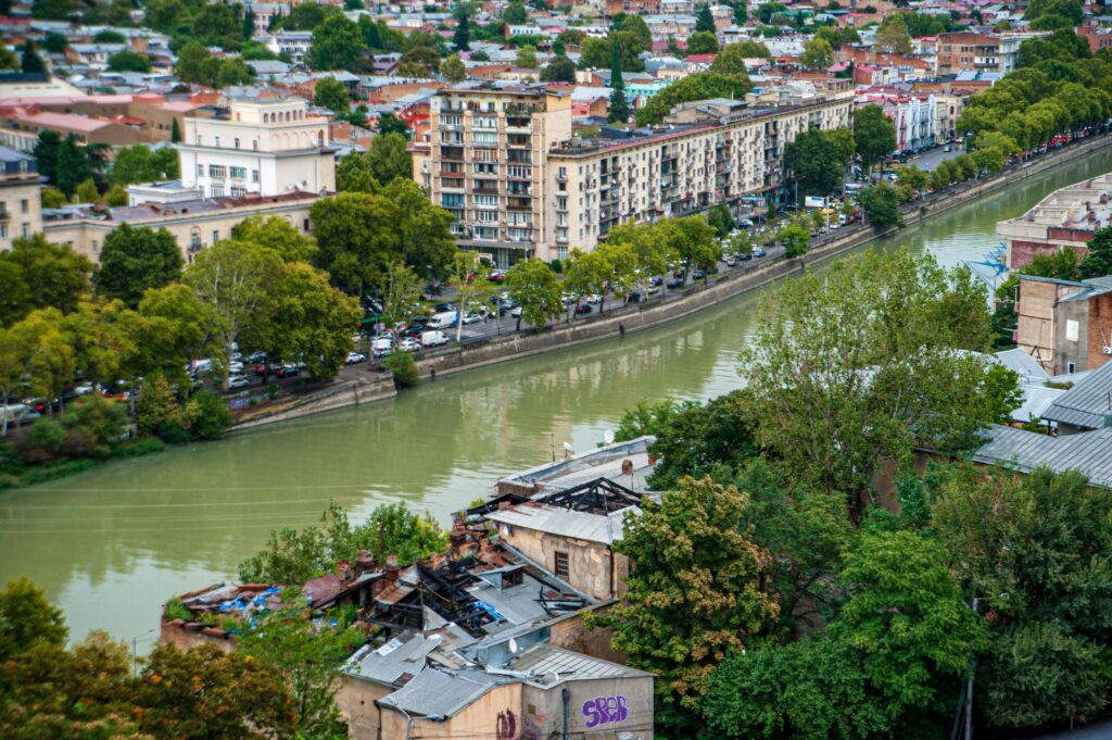 View of Tbilisi, Georgia, with the Mtkvari River flowing through the city, surrounded by historic buildings and green urban landscapes