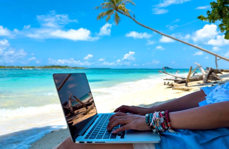 Digital nomad working on a laptop from a tropical beach, exploring places similar to Bali but cheaper