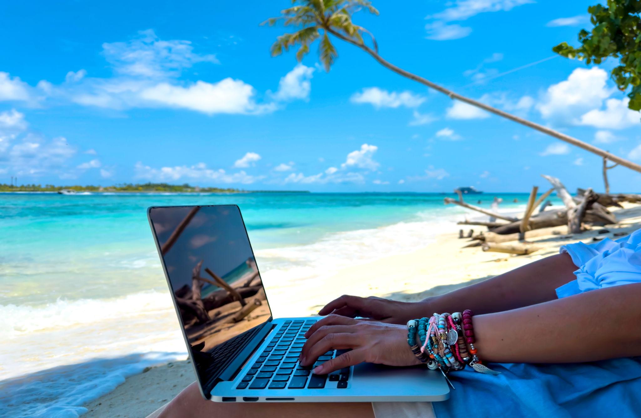 Digital nomad working on a laptop from a tropical beach, exploring places similar to Bali but cheaper
