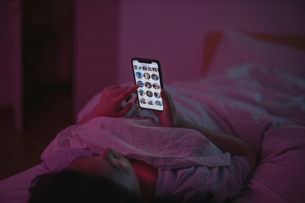 Person lying in bed scrolling social media on a smartphone, illustrating parasocial relationships, influencer culture and digital loneliness.
