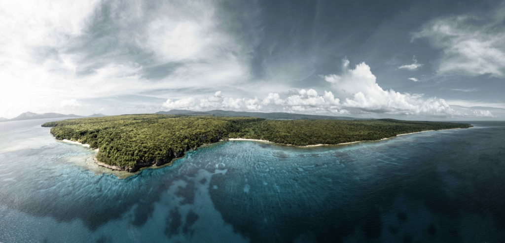 Aerial view of the coastline and tropical forest in Vanuatu with crystal-clear blue water.