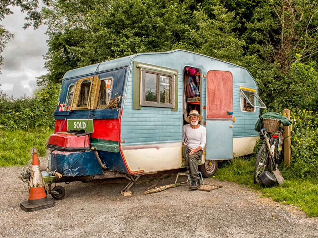 Senior traveller sitting outside a vintage caravan, representing the grey nomad lifestyle and long-term road travel.