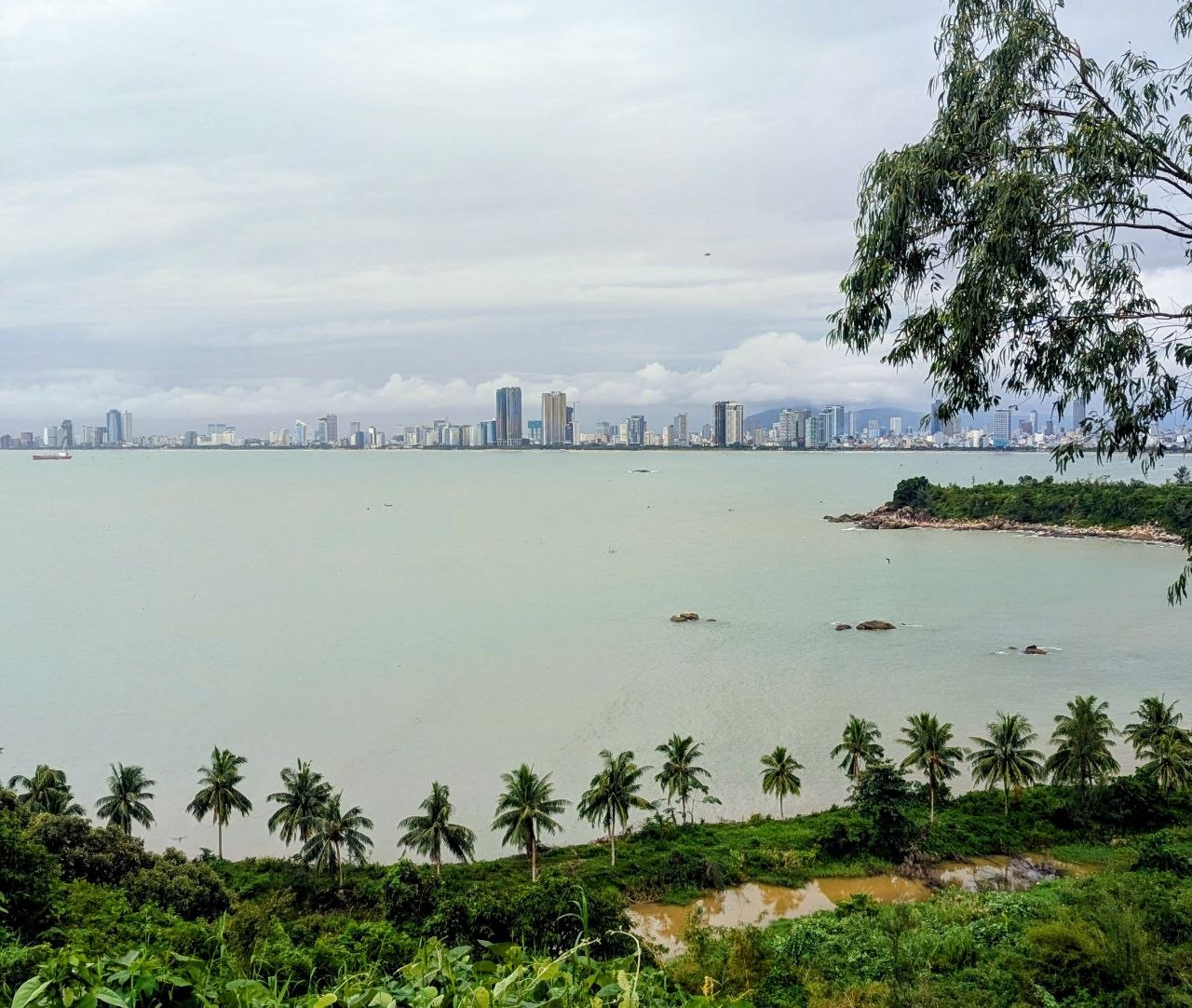 Panoramic view of Da Nang, Vietnam, showing the coastline, palm trees, and the city's modern skyline along the South China Sea.