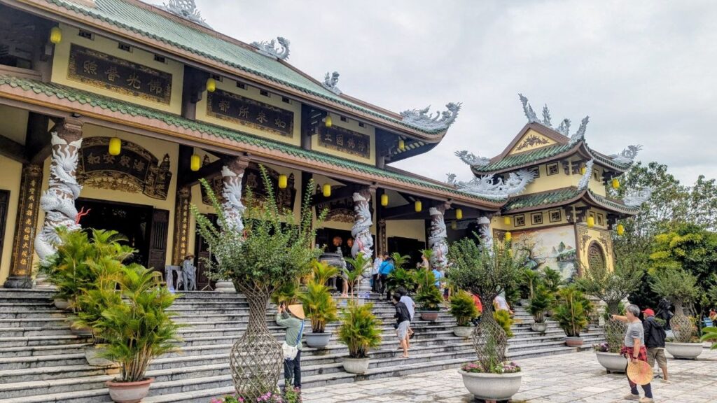 Traditional Buddhist temple in Vietnam featuring ornate architecture, stone steps, and visitors exploring the peaceful temple grounds.