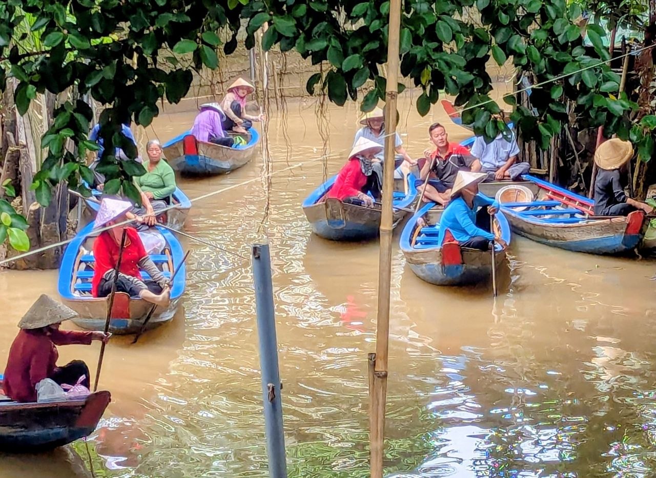 Traditional floating market in Vietnam with local vendors paddling wooden boats along a narrow river surrounded by lush tropical vegetation.