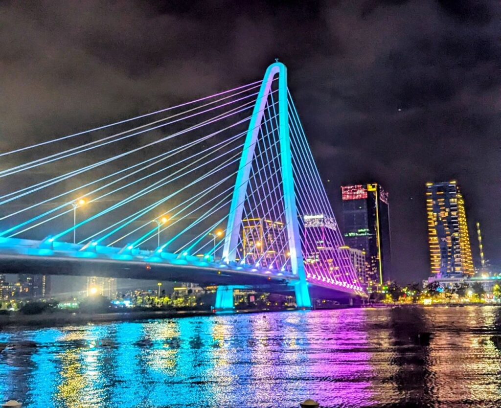 Ba Son Bridge illuminated at night over the Saigon River in Ho Chi Minh City, Vietnam, with the modern skyline reflected in the water.