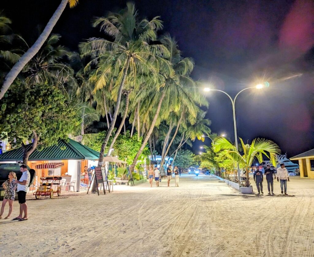 Evening walk along the main street of Maafushi Island in the Maldives with palm trees, cafés and local shops.