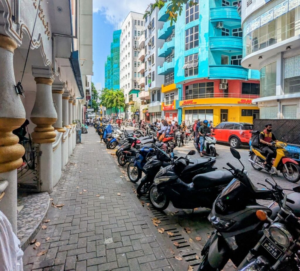 Street in Malé, the capital of the Maldives, lined with motorbikes, colorful buildings and local businesses.