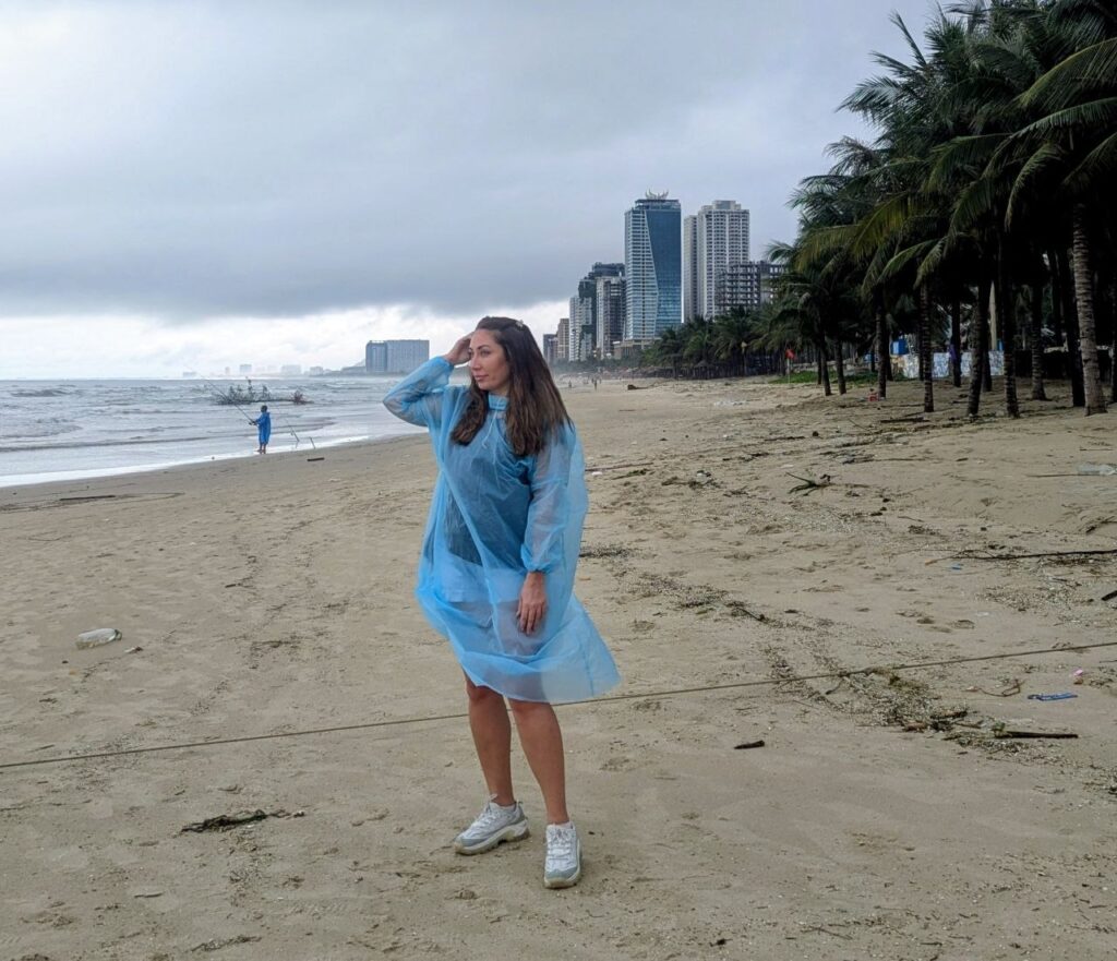 Woman wearing a rain poncho on Da Nang Beach during heavy rain in late September, with rough sea and unsafe swimming conditions