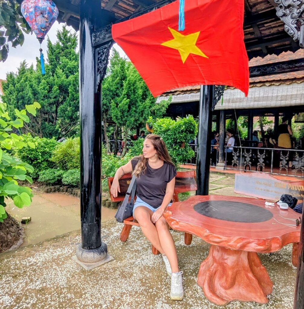 Woman sitting beneath the Vietnamese flag at a traditional café in Vietnam