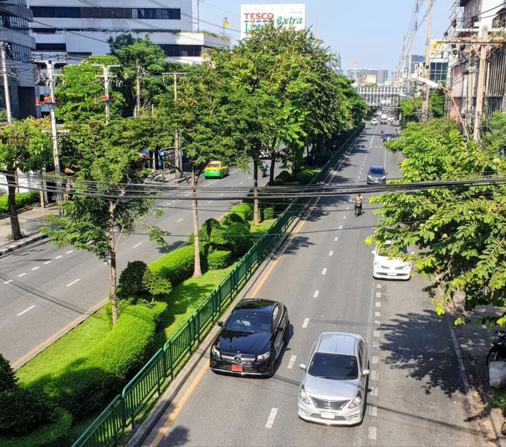 Tree-lined street in Bangkok with light traffic, green median and residential buildings