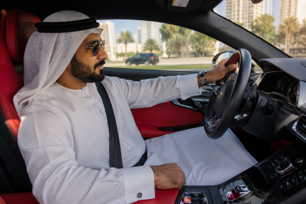 Emirati man wearing a traditional white kandura and ghutra driving a luxury sports car in Dubai.