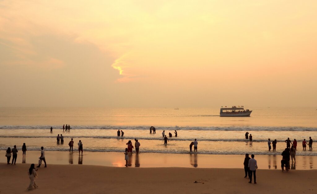 Sunset at a beach in Goa, India, with people walking along the shoreline.