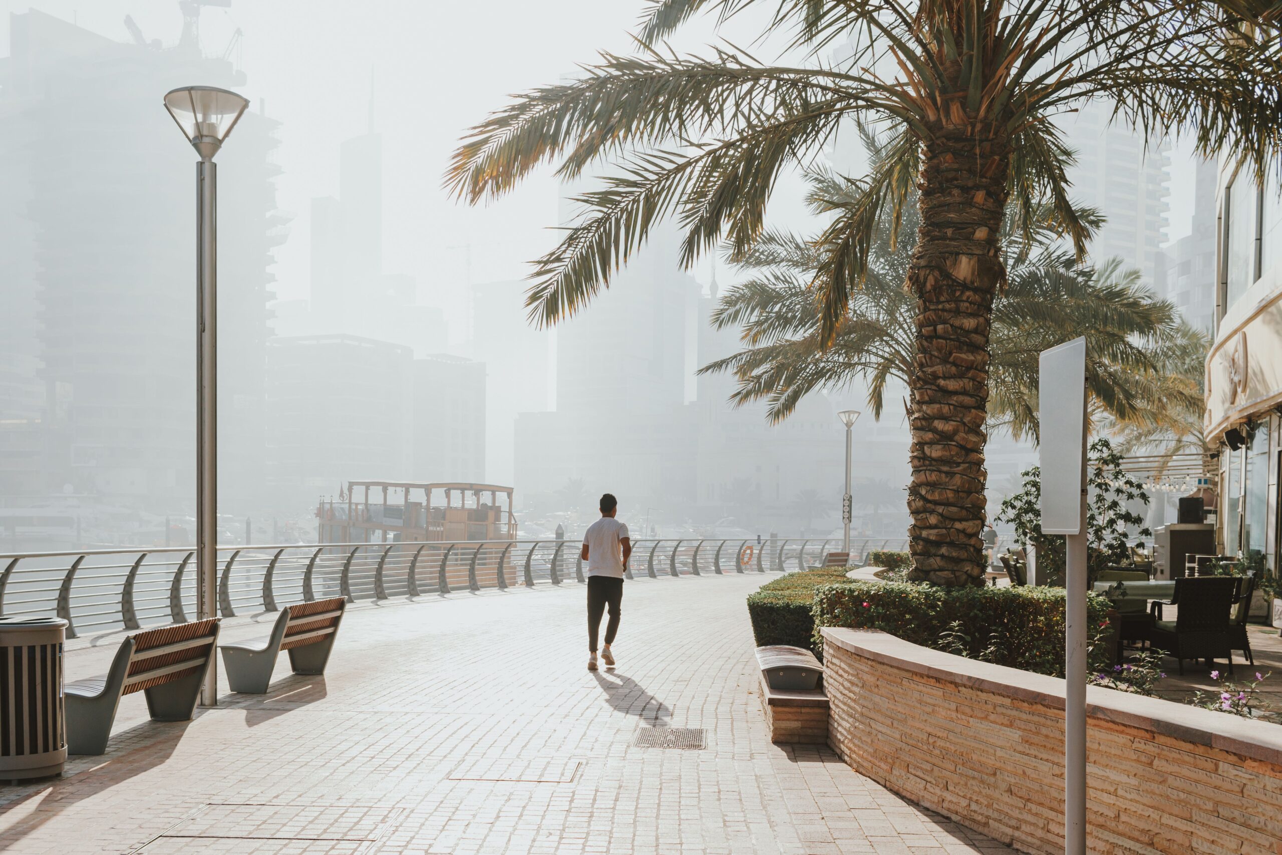 Dubai Marina promenade on a hot and hazy summer morning lined with palm trees and waterfront cafés in Dubai, UAE