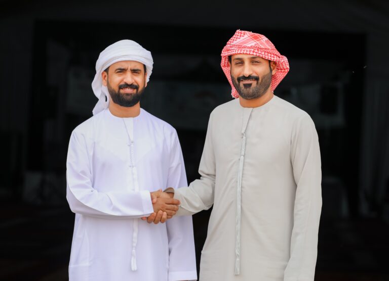 Two Emirati men wearing traditional kanduras and head coverings greeting each other with a handshake in the UAE.