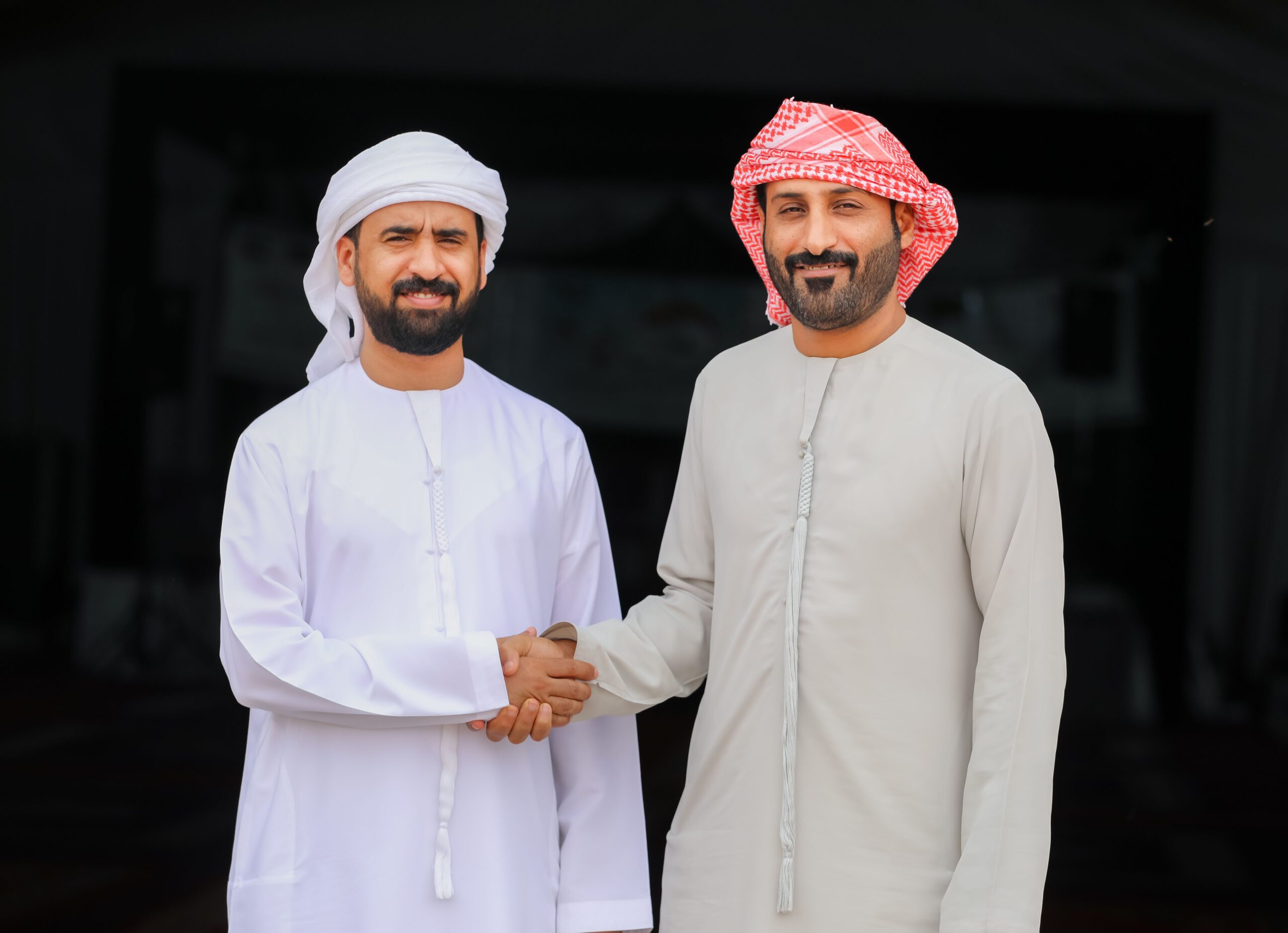 Two Emirati men wearing traditional kanduras and head coverings greeting each other with a handshake in the UAE.