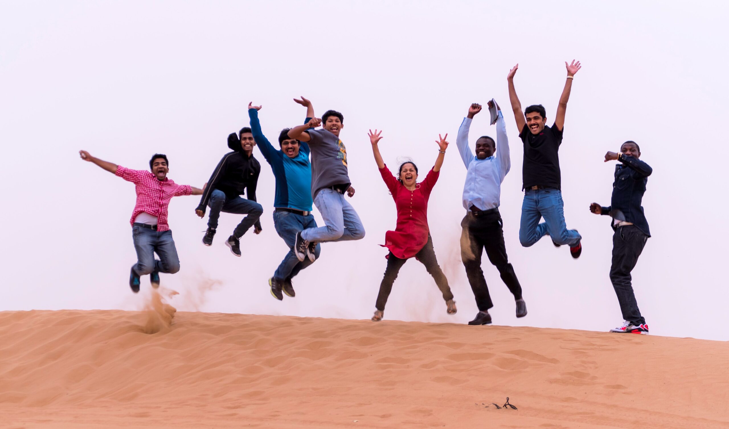 Group of people jumping on sand dunes in the Dubai desert, representing the multicultural community of the UAE.