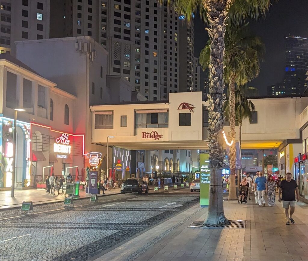 The Walk at JBR in Dubai on a warm summer night with restaurants, palm trees, pedestrians and illuminated high-rise buildings