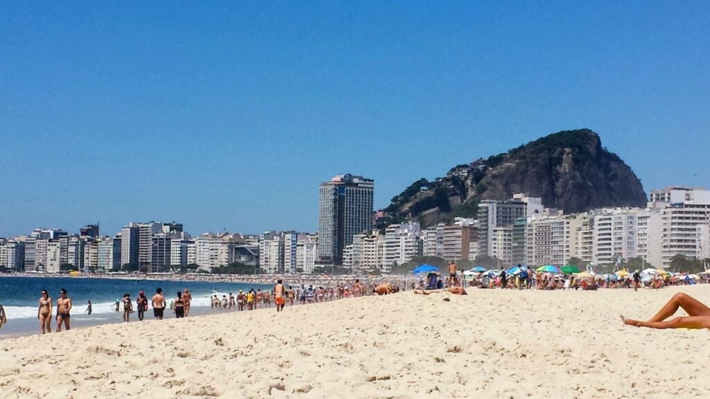 Copacabana Beach in Rio de Janeiro, Brazil, with beachgoers and city buildings along the coastline