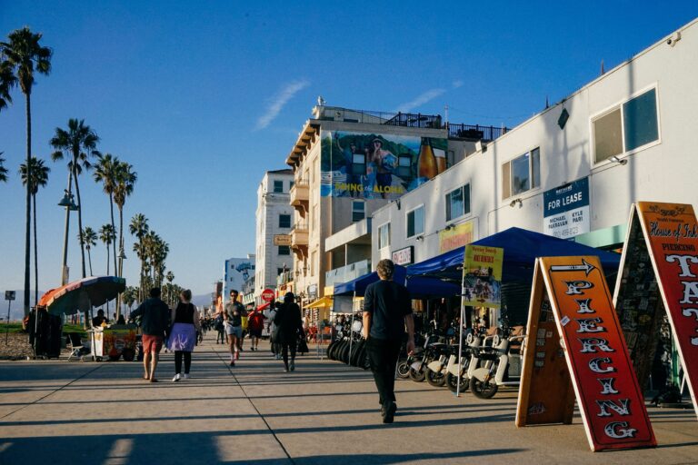 People walking along Venice Beach Boardwalk in Los Angeles, with palm trees and beachfront shops
